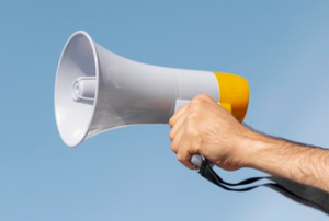 Op de foto zie je een hand die een megafoon vasthoudt. Laat je stem horen! Klik op dit blok voor meer informatie over waarom je moet stemmen.