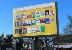 Op de foto zie je een verkiezingsbord met posters van politieke partijen. Klik op dit blok voor meer informatie over de politieke partijen.